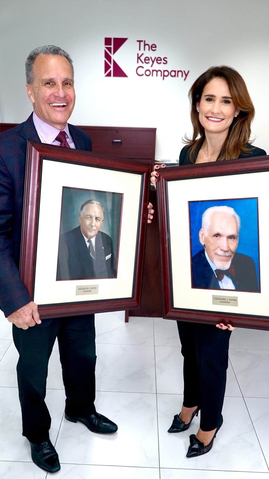 Keyes Company leadership holding portraits of founder Kenneth S. Keyes and chairman Theodore J. Pappas